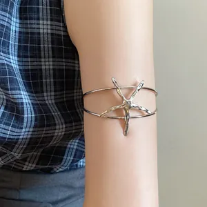 Detailed macro view of a silver-toned metal starfish open armlet jewelry on a model's arm