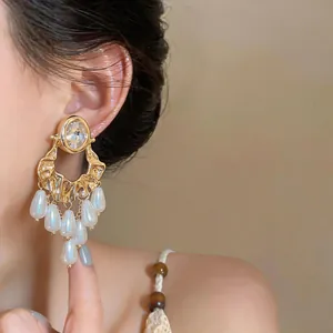 Detail of statement earrings featuring an oval crystal and dangling pearl tassels.