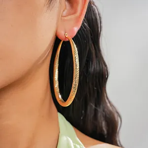Model wearing large textured gold-toned hoop earrings with elegant faceted geometric surface