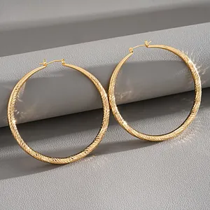 Close-up detail of large gold hoop earrings with elegant textured diamond-cut surface pattern