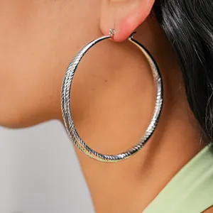 Detailed view of large silver metal hoop earrings featuring a faceted textured surface finish