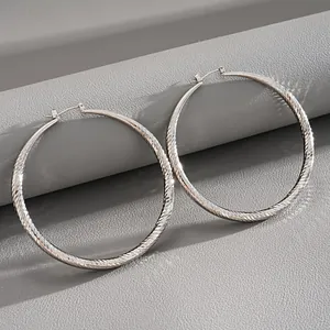 Close-up detail of silver-tone large hoop earrings with elegant diamond-cut texture
