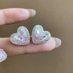 Dettaglio degli orecchini a cuore in madreperla con motivo a farfalla e incisioni argentate