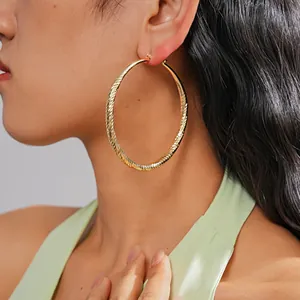 Close-up of a model wearing large gold-toned faceted hoop earrings with textured finish