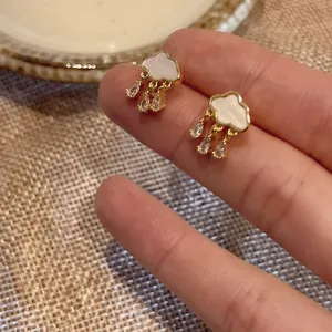 Close-up of gold cloud earrings with white shell inlay and waterdrop zircons