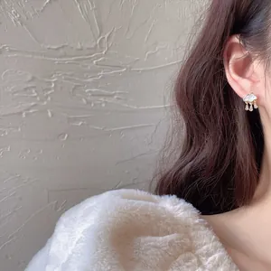Close-up of mother-of-pearl cloud earrings with zircon teardrops on an ear.