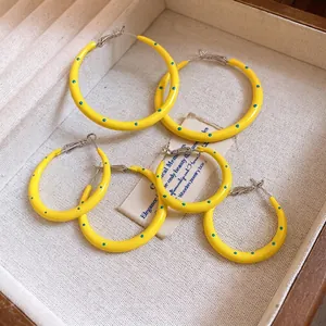 Vibrant yellow enamel hoop earrings with blue polka dots in a jewelry box.
