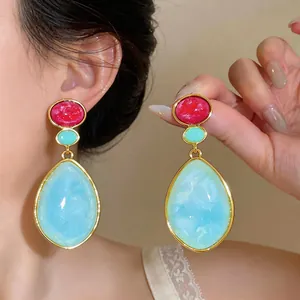 Primer plano de pendientes largos de resina vintage en rojo y azul, mostrados puestos en la oreja.