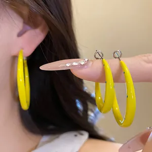 Detail of yellow enamel C-shaped hoop earrings with blue polka dots on a silver needle.