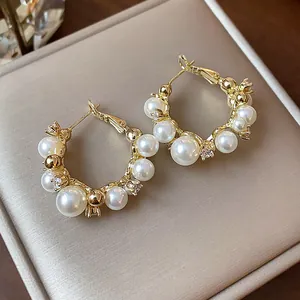 Vue détaillée de boucles d'oreilles créoles dorées avec perles blanches et zircons.