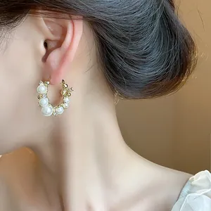 Gros plan de boucles d'oreilles créoles dorées 14 carats avec perles et zircons sur modèle.