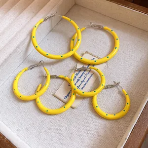 Detail showing yellow spotted C-shaped hoop earrings with blue polka dots in jewelry box