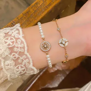 Détail montrant deux bracelets en or et perles avec étoiles sur un poignet en dentelle.