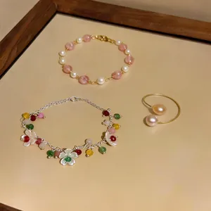 Dettaglio di braccialetti con perline colorate e anello con perle su vassoio crema.