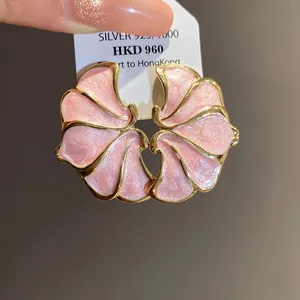 Detailed macro view of pink enamel flower stud earrings with gold edges and silver needles.
