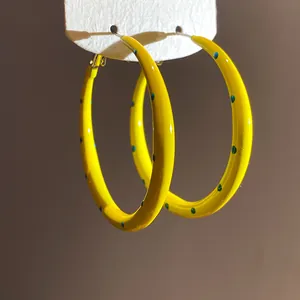 Detailed macro view of vibrant yellow enamel polka dot C-shaped hoop earrings on white display card
