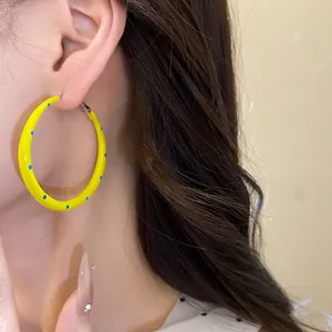 Close-up view of yellow C-shaped hoop earrings with blue polka dots worn by a model