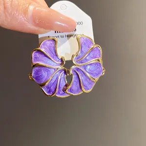 Macro view of purple dripping oil flower stud earrings with gold trim on a white card