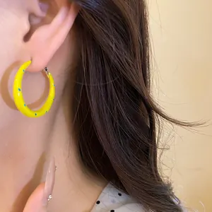 Detail view of vibrant yellow C-shaped hoop earring with blue dots on a model ear.