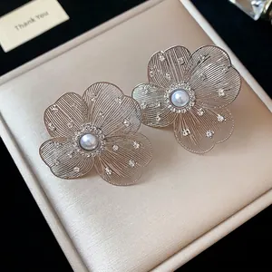 Elegant hollow flower earrings with pearls and rhinestones on a beige gift box.
