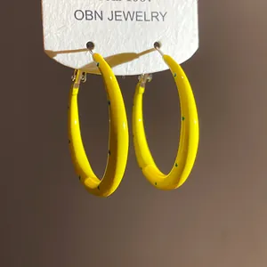 Close-up of yellow enamel C-shaped hoop earrings with blue polka dots and silver pins.