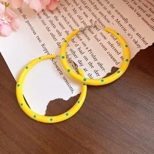Close-up of yellow enamel hoop earrings with blue polka dots on a wooden background