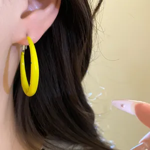 Close-up detail of a bright yellow C-shaped enamel hoop earring with blue polka dot patterns