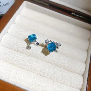 Macro view of sparkly blue square crystal ear cuffs displayed in a white velvet jewelry box