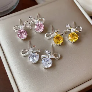 Primo piano di eleganti orecchini a lobo con fiocco e zirconi rosa, gialli e chiari.