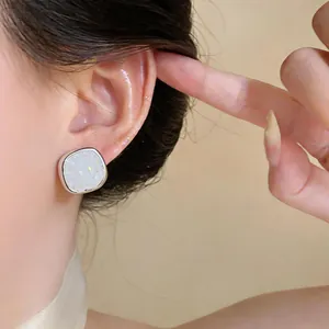 Close-up of a minimalist zircon stud earring with white glittery inlay worn on the ear.