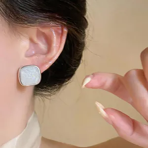 Close-up shot of a minimalist square stud earring with white resin and gold glitter flecks
