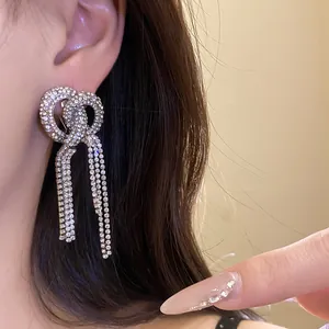 Detail view of sparkling rhinestone bowknot tassel drop earrings worn on a model's ear