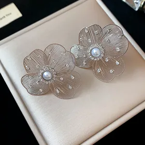 Detailed close-up of silver hollow flower stud earrings with pearl and rhinestones
