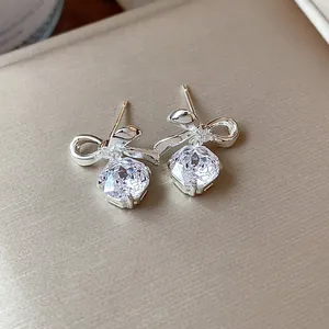 Primo piano di eleganti orecchini a lobo con fiocco d'argento e zirconi tondi scintillanti.