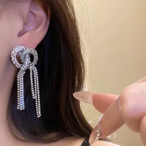 Close-up detail of luxury full rhinestone bow knot tassel earrings worn on a person ear