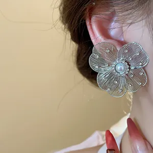 Close-up of elegant hollow flower earring with pearl center and rhinestones