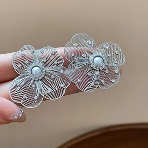 Detail view of hollow filigree silver flower earrings with central pearl and crystals.
