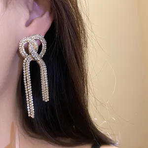 Close-up of sparkling long tassel earrings with rhinestone bow design on model