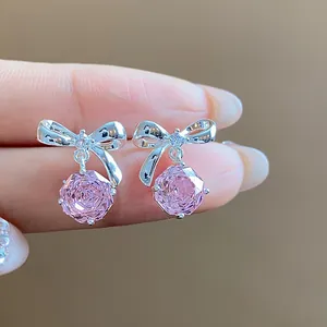 Dettaglio macro di orecchini a fiocco in argento con cristalli rosa a forma di fiore.