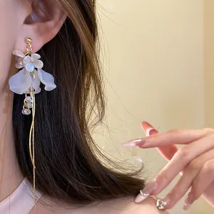 Nahaufnahme eleganter Ohrringe mit weißen Blüten und goldenen Quasten an einem Model