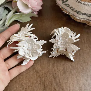 Detailed view of white leather flower earrings with pearl centers on a wooden surface.