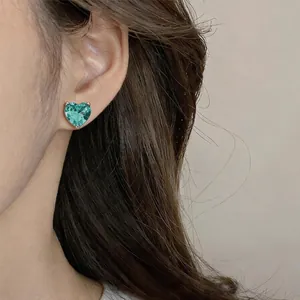 Gros plan d'une boucle d'oreille en zircone coeur bleu sarcelle sur une oreille