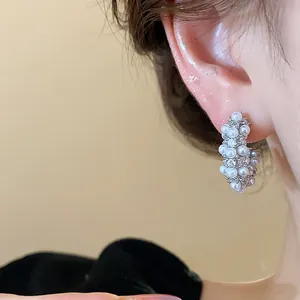 Macro detail of elegant French style C-shaped earrings with pearls on a model ear.