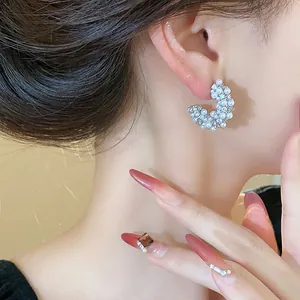 Detailed close-up of French style C-shaped pearl earrings with sparkling crystals.