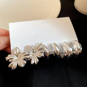 Detailed view of silver-tone flower studs and textured hoop earrings on white display card.