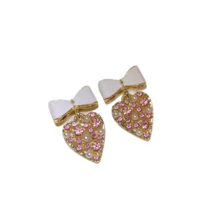 Boucles d'oreilles nœud et cœur avec strass roses et perles sur monture dorée.