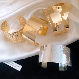 Close-up of gold and silver irregular cuff bracelets with engraved floral patterns.