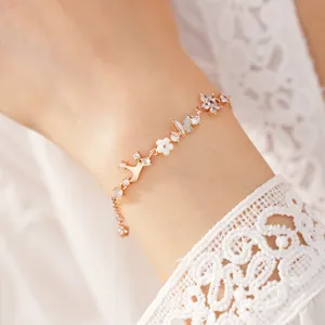 Close-up of gold bracelet with zircon, shell butterfly and flower charms on wrist