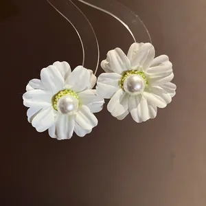 Detailed macro view of white fabric flower earrings featuring a glossy pearl center