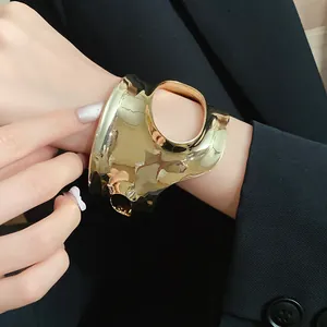 Detailed view of an irregular pleated gold cuff bracelet worn on a woman's wrist.